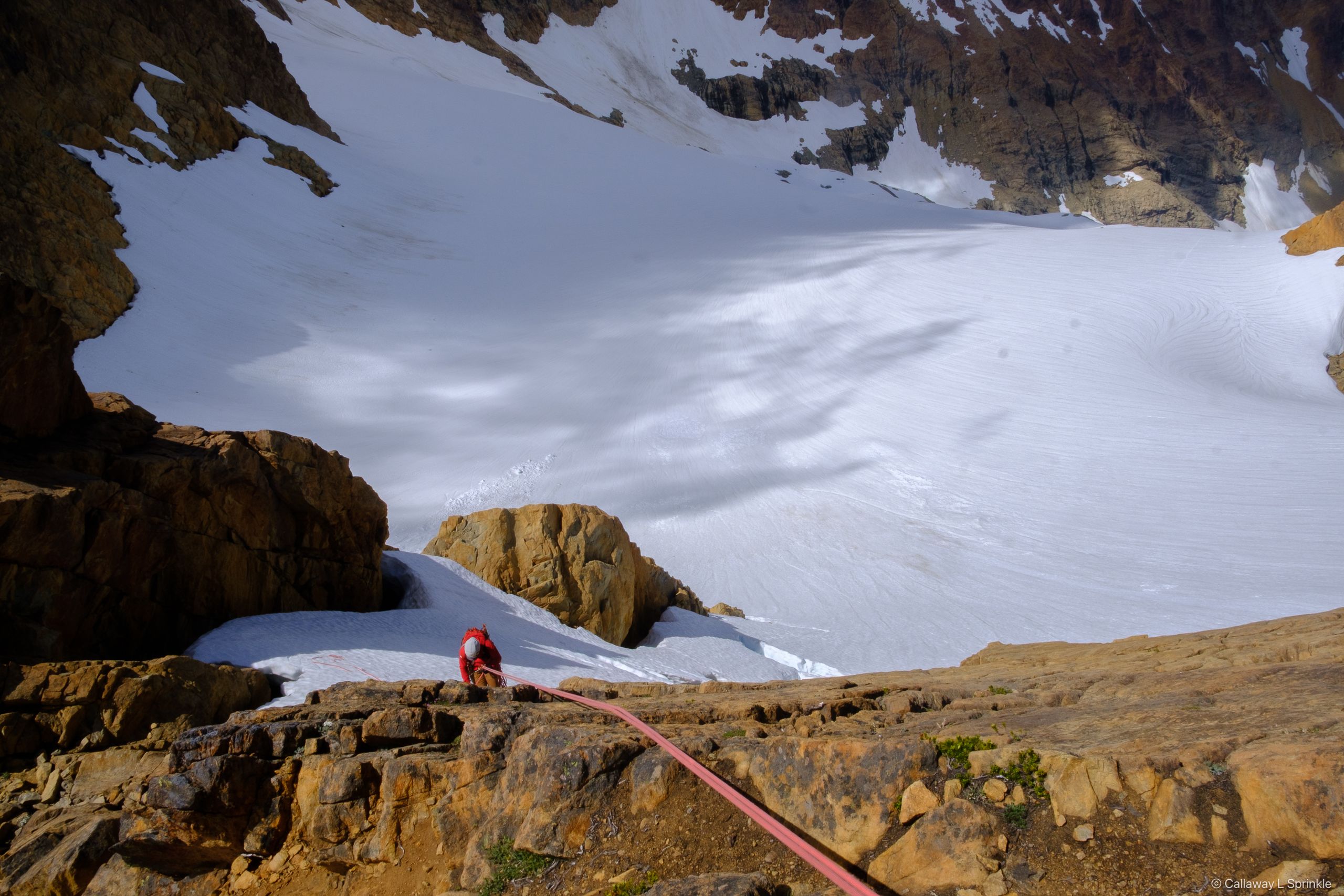 Looking down from a belay stance onto the glacier far below, a rope running to a climber on a ledge